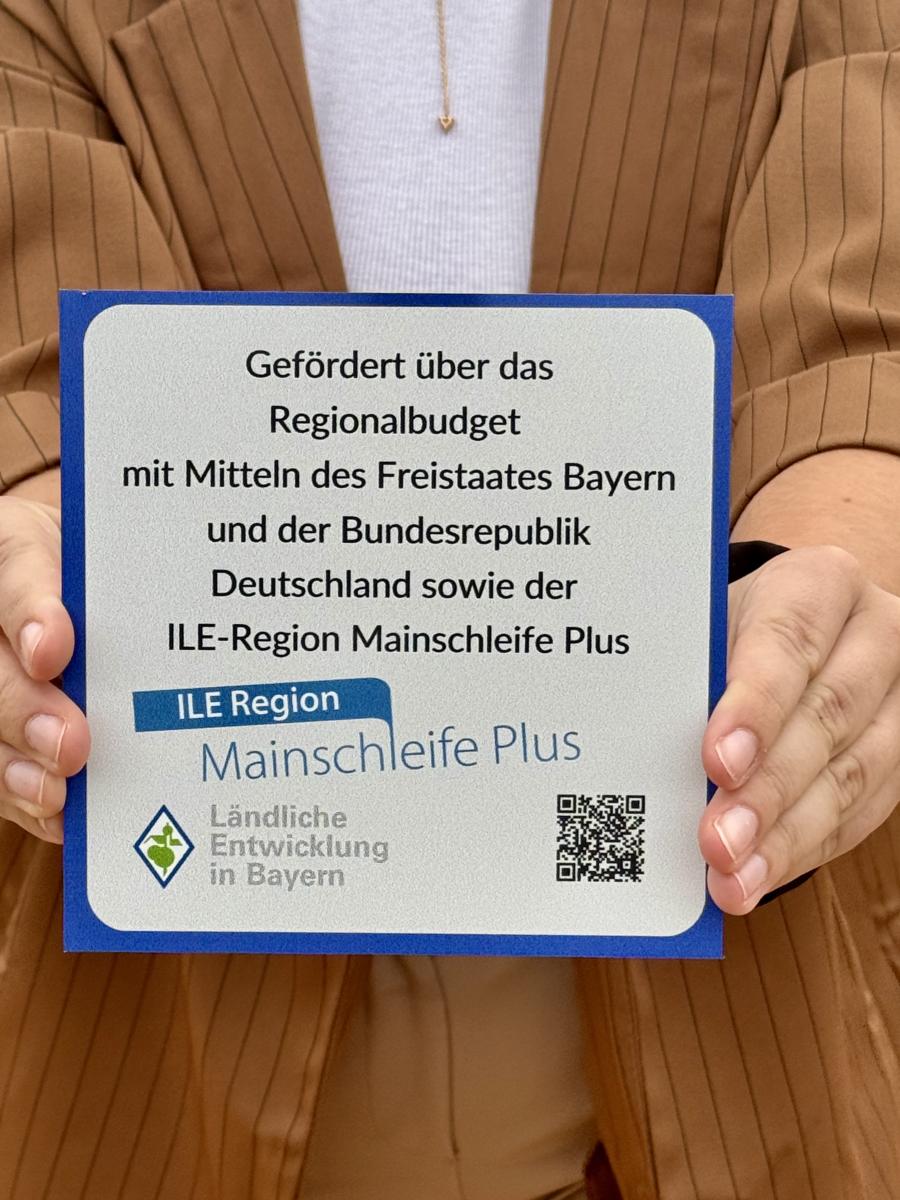 Eine Person hält ein Förderschild zum Regionalbudget in der Hand