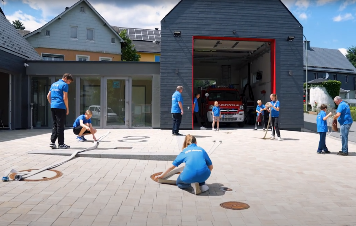 Jugendliche in blauen einheitlichen Shirts absolvieren Feuerwehrübungen auf dem Vorplatz.