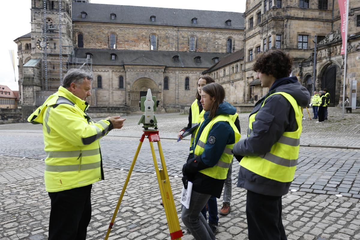 Ein Mann und drei Jugendliche mit einem Tachymeter, der Dom im Hintergrund