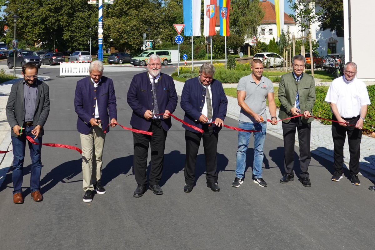 Mehrere Personen stehen auf einer Straße und schneiden ein Band zu Einweihung durch.