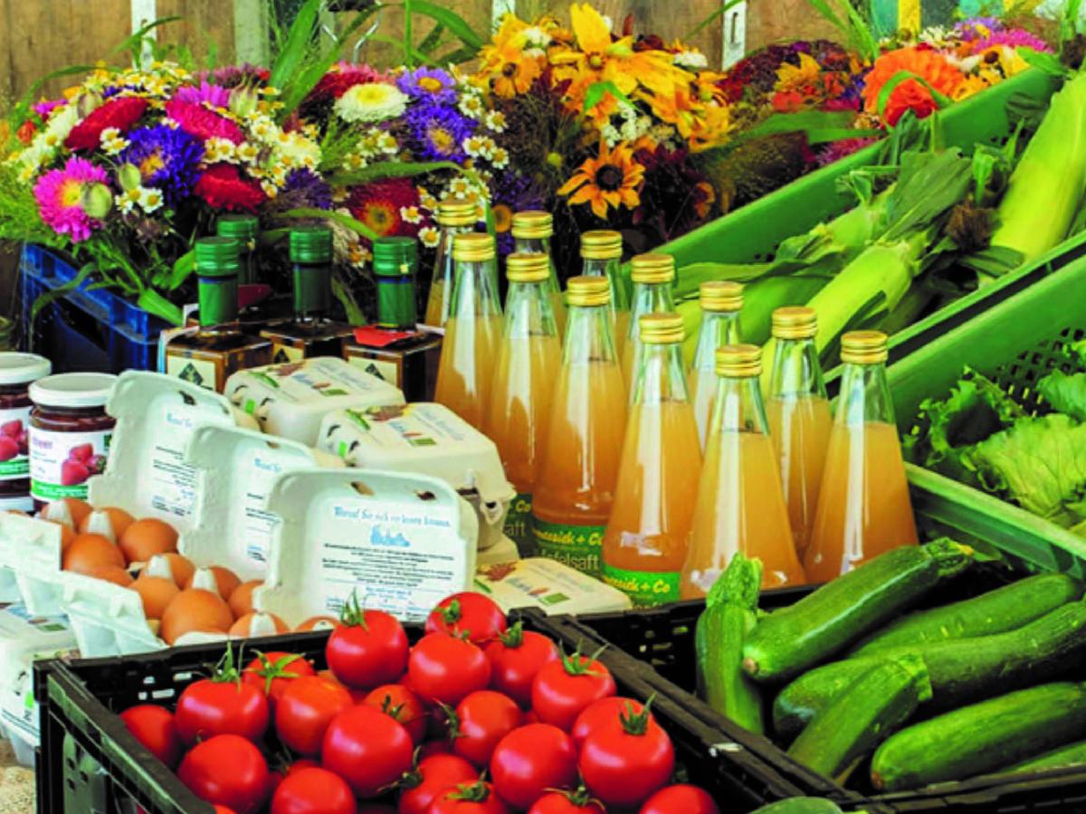 Buntes Sortiment an frischen Waren wie Gemüse, Eier, Saft und Blumen.