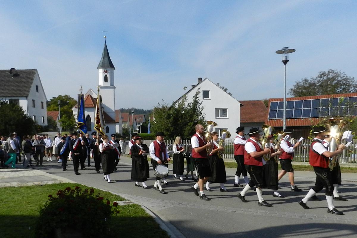 Festzug mit Musikern, im Hintergrund die Dorfkapelle.