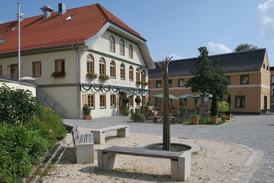 EIn großes Wirtshaus, davor ein Platz mit Brunnen.