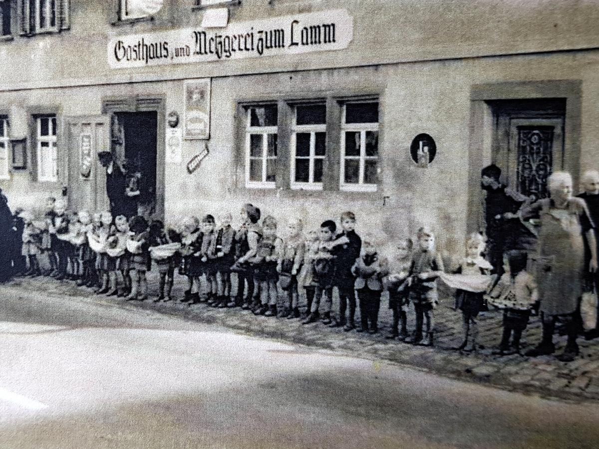 Auf dem historischen Foto steht eine Reihe Kinder vor dem alten Gasthaus zum Lamm und warten darauf, dass Ihnen die Hochzeitsleute "Süßigkeiten" zuwerfen.