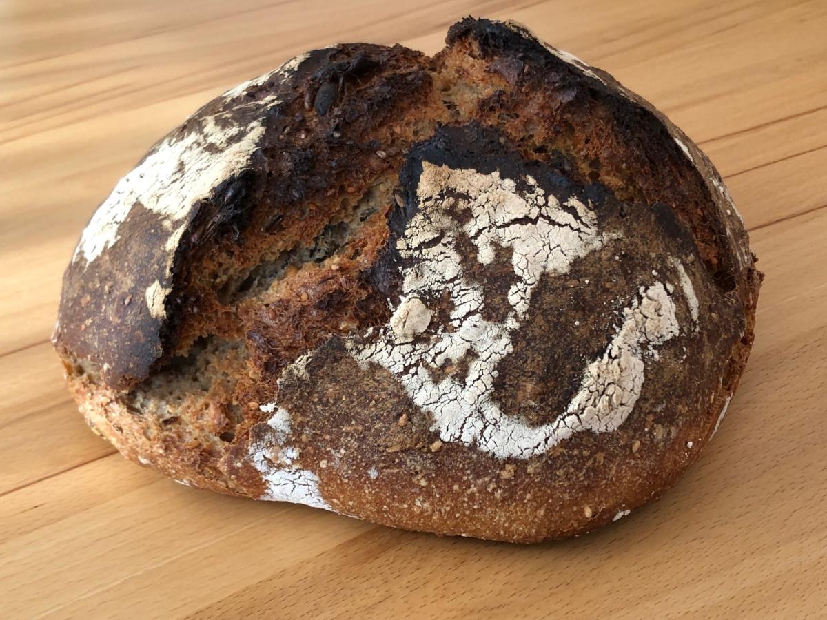 Ein Dinkelbrot mit aufgerissener Kruste liegt auf einer Holzplatte.