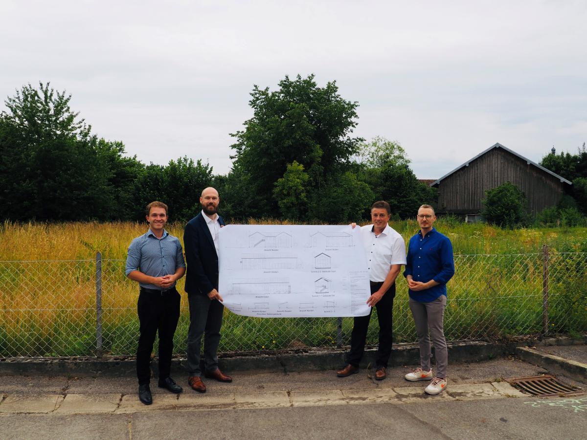 Vier Herren stehen auf dem Baugrund für das neue Oberschneidinger Schulhaus und halten einen Bauplan in ihren Händen.