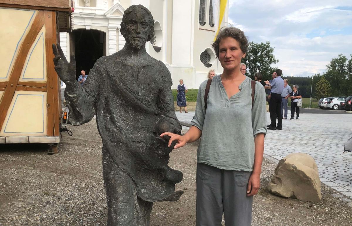 Künstlerin steht neben einer Christus-Skulptur